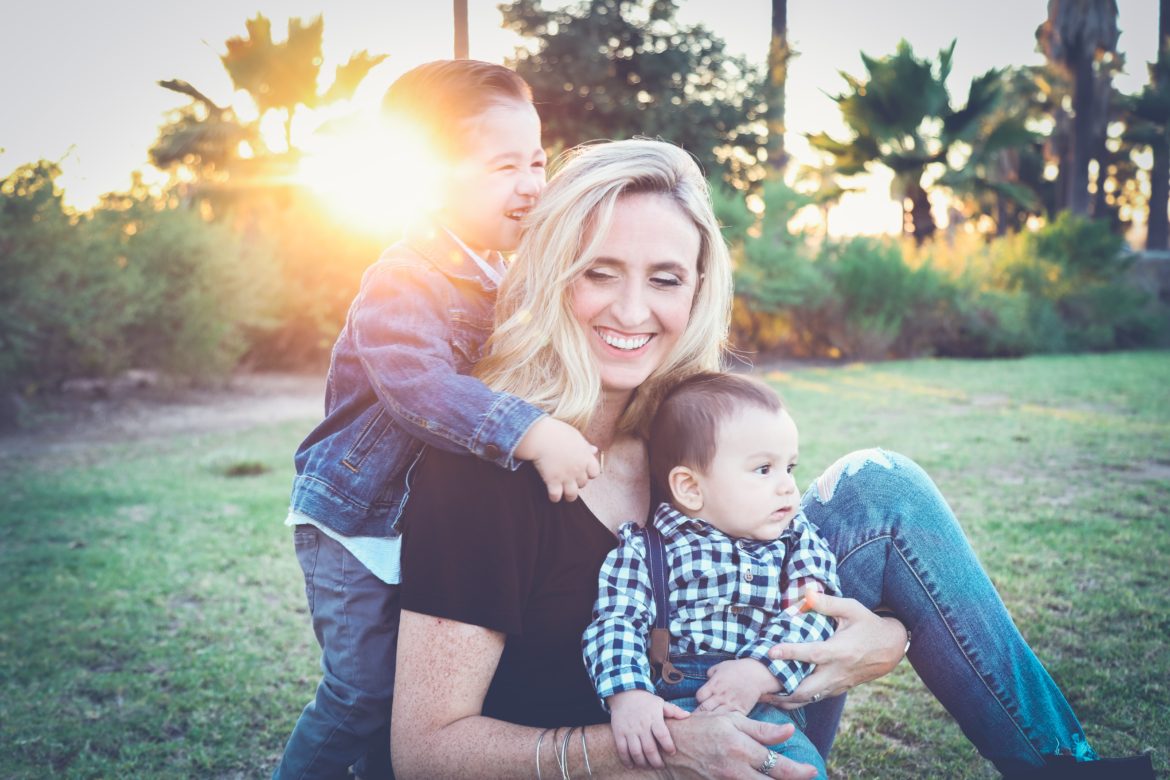 photo of a lady with two children and the sun setting or maybe rising behind her