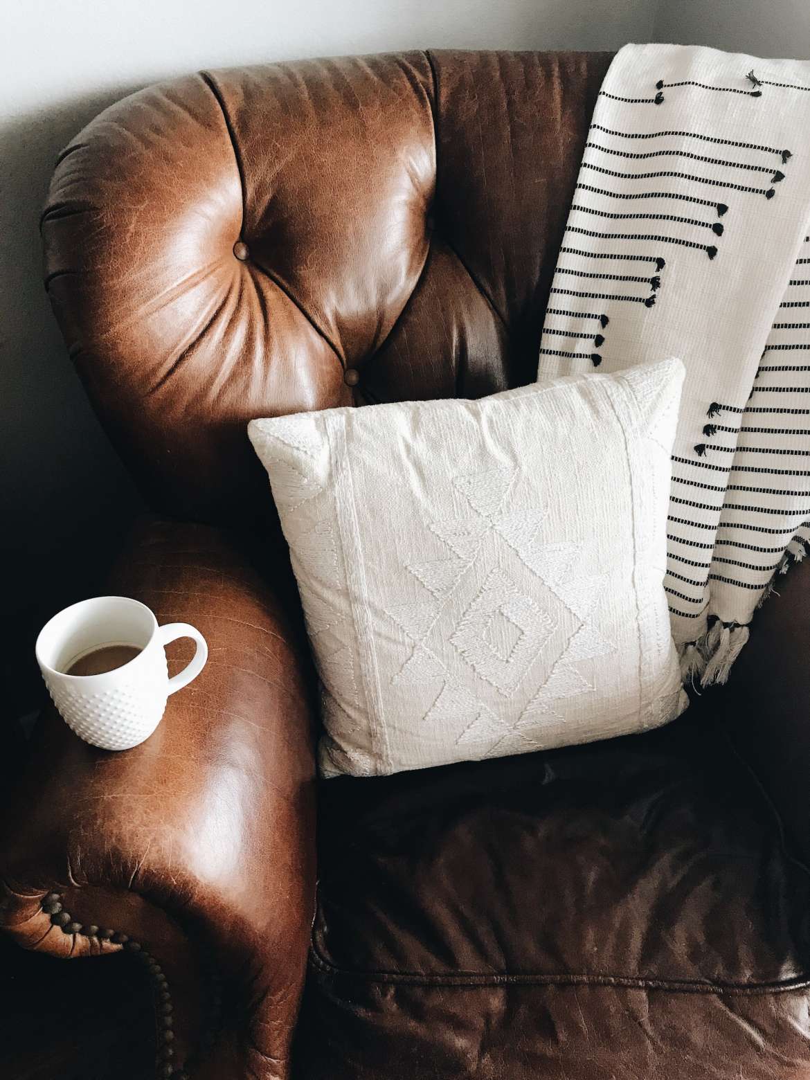 brown chair with pillow in it. blanket over back. coffee cup on arm