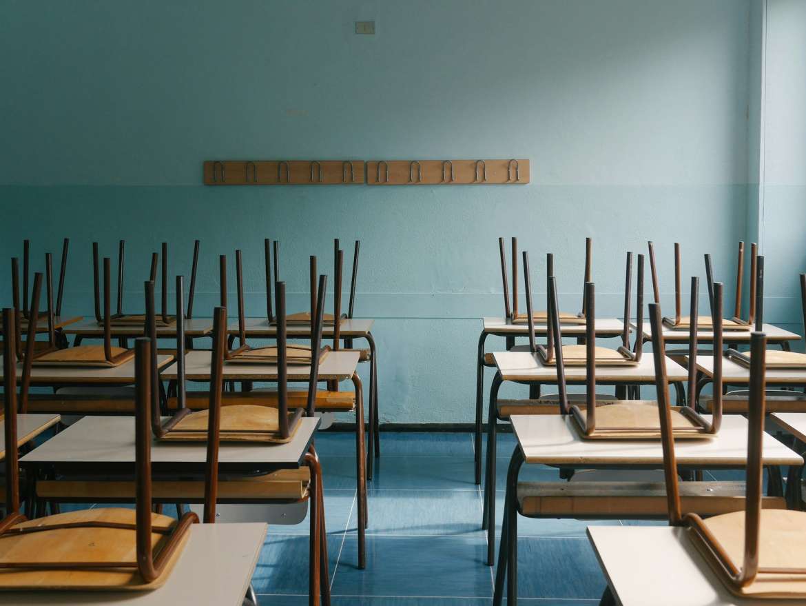 empty school room. blue wall. chairs stacked upside down on school desks.